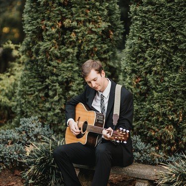Reagan seated with his guitar beside a boxwood hedge