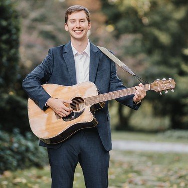Reagan Leonard playing acoustic guitar on a garden path