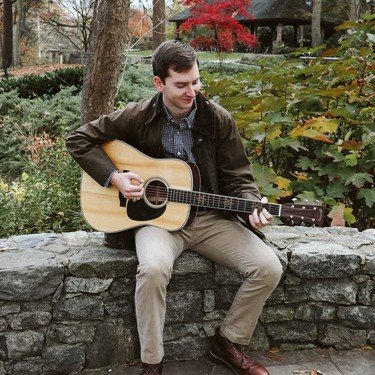 Reagan playing guitar beside a stone wall in autumn