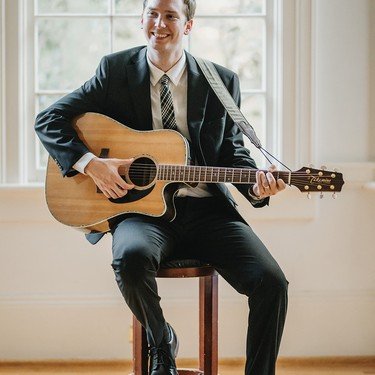 Reagan playing guitar on a stool indoors